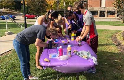 Group of students painting rocks on a table outside