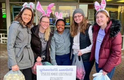 Students participating in Easter Egg Hunt, wearing bunny ears and holding bags of eggs.